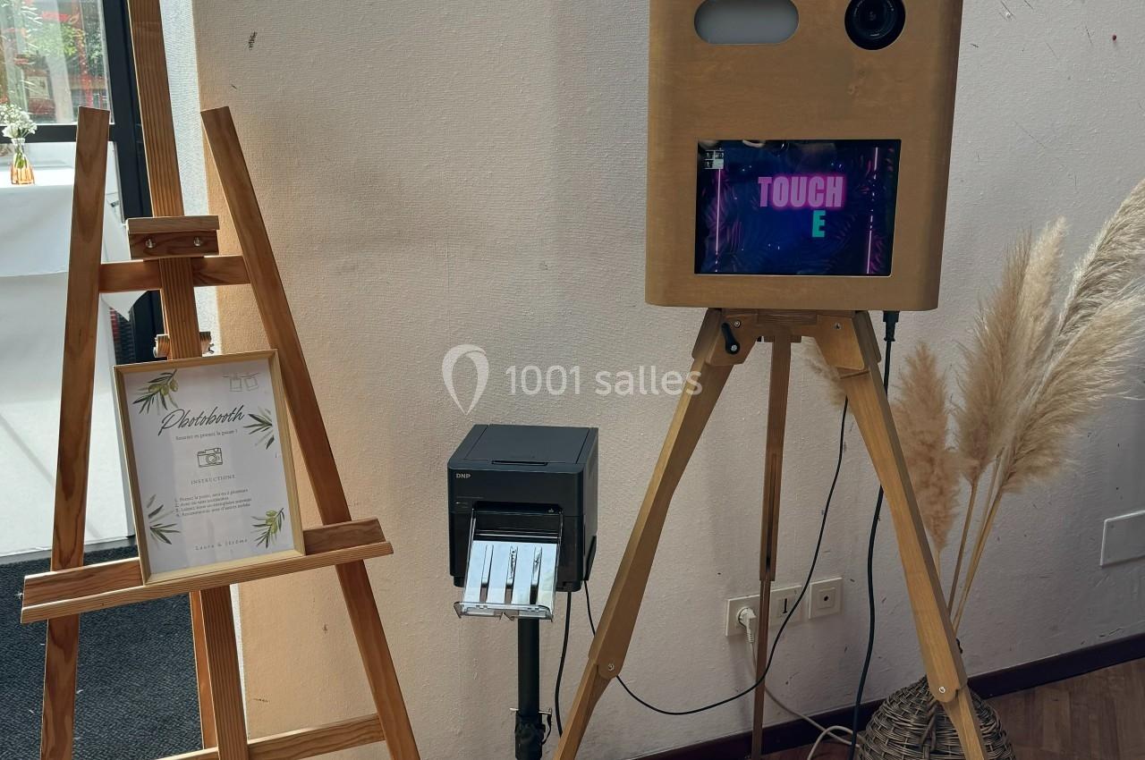 Borne photo en bois sur trépied avec écran tactile, imprimante et anneau lumineux, près d'un chevalet et d'une décoration en…