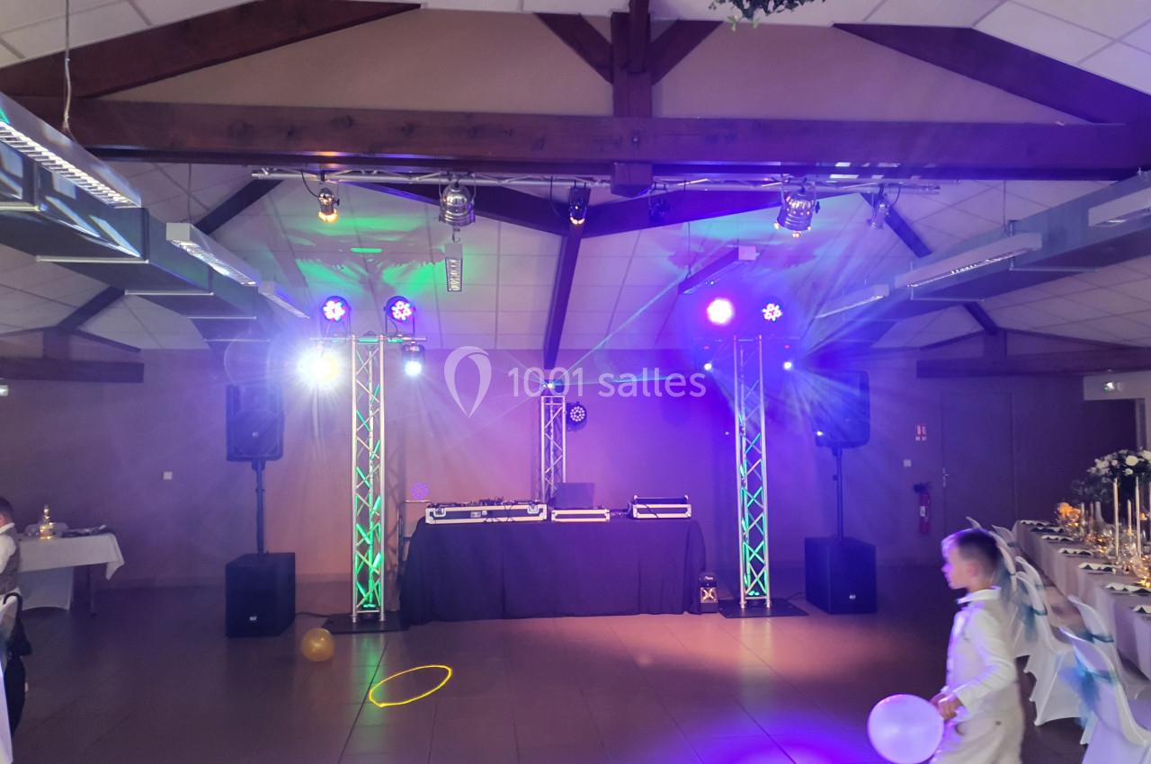 Salle de réception décorée avec éclairage coloré, piste de danse vide et matériel de DJ installé au fond.