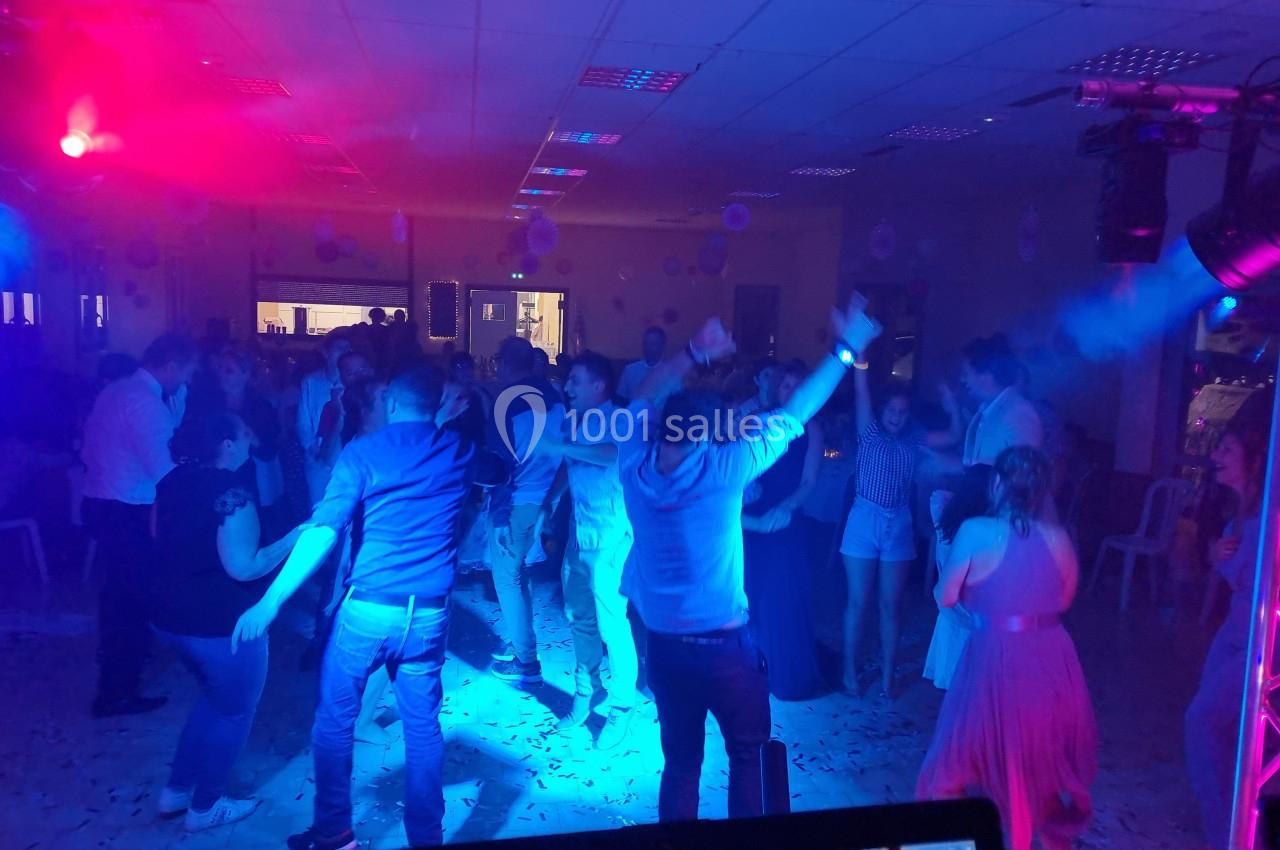 Personnes dansant sous des éclairages colorés dans une salle, ambiance festive avec musique et décorations.