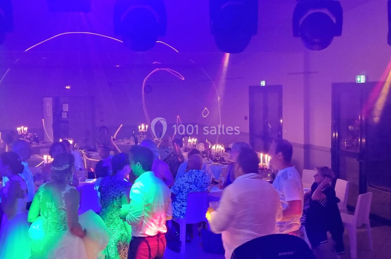 Des invités dansent et discutent dans une salle de réception éclairée par des lumières colorées et des bougies.