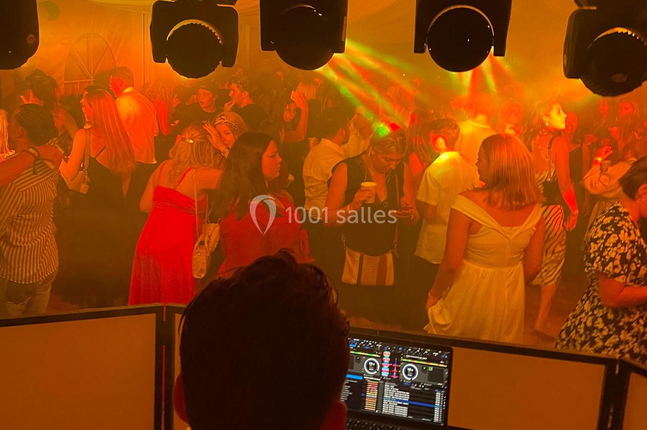 Vue depuis la cabine d’un DJ sur une foule dansante sous des lumières colorées dans une ambiance festive.