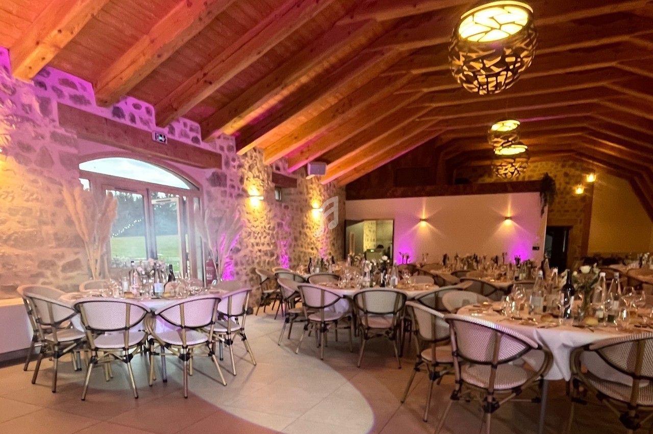 Salle de réception en pierre avec plafond en bois, tables rondes dressées et éclairage chaleureux.