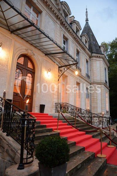 Façade d'un bâtiment élégant avec escalier en pierre, tapis rouge et balustrades en fer forgé, éclairé en soirée.