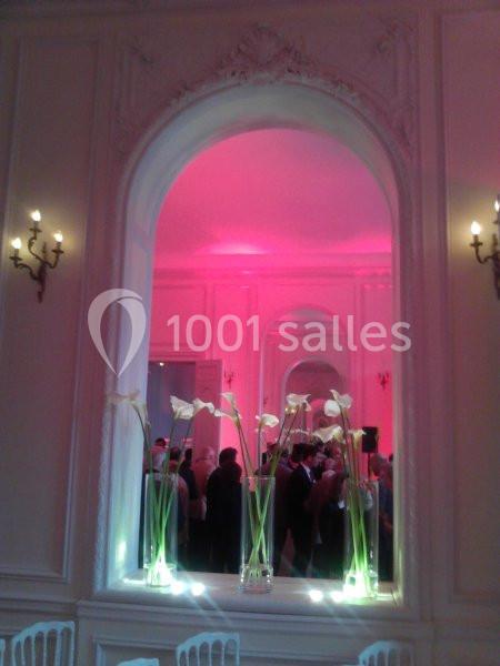 Des vases avec des arums blancs alignés devant un grand miroir dans une salle éclairée par une lumière rose.
