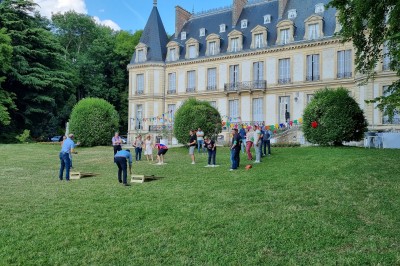 Façade d'un château illuminé la nuit avec une fontaine ornée de statues au premier plan.