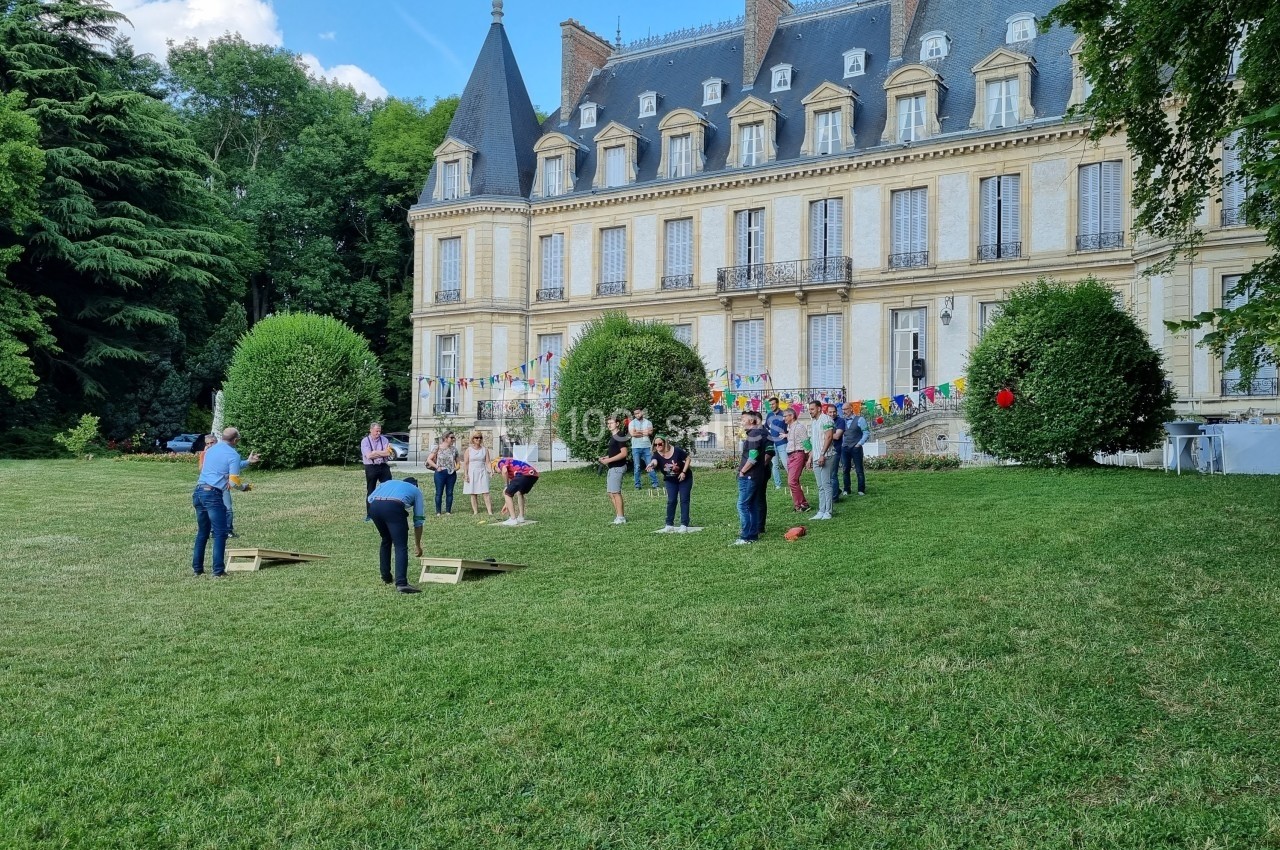Personnes jouant à des jeux en plein air sur une pelouse devant un château entouré de verdure.