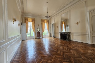 Façade d'un château illuminé la nuit avec une fontaine ornée de statues au premier plan.