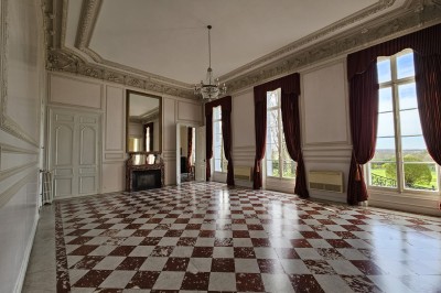 Façade d'un château illuminé la nuit avec une fontaine ornée de statues au premier plan.