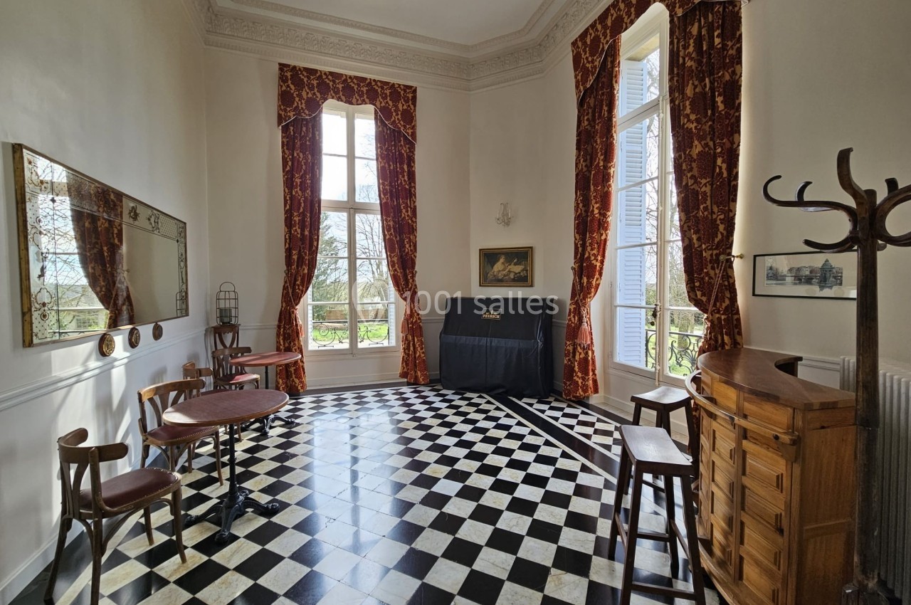Salle lumineuse avec sol en damier, grandes fenêtres, rideaux rouges, piano noir et mobilier en bois.