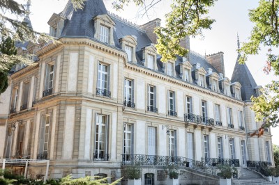 Façade d'un château illuminé la nuit avec une fontaine ornée de statues au premier plan.