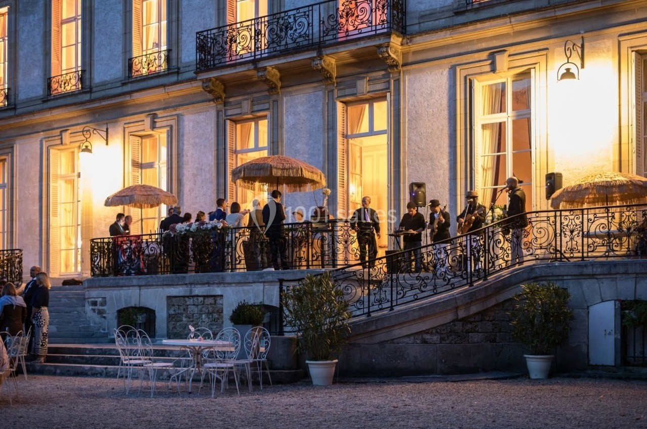 Groupe de personnes rassemblées sur une terrasse éclairée d'un bâtiment élégant au crépuscule.