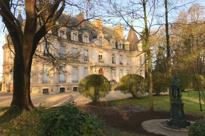 Façade d'un château illuminé la nuit avec une fontaine ornée de statues au premier plan.