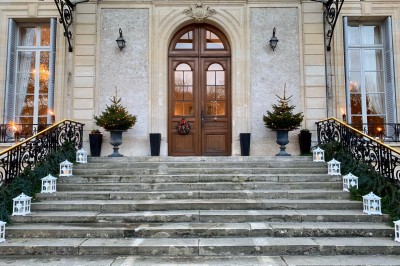 Façade d'un château illuminé la nuit avec une fontaine ornée de statues au premier plan.