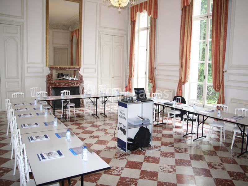 Salle de réunion lumineuse avec tables disposées en U, chaises blanches, matériel de présentation et grandes fenêtres.