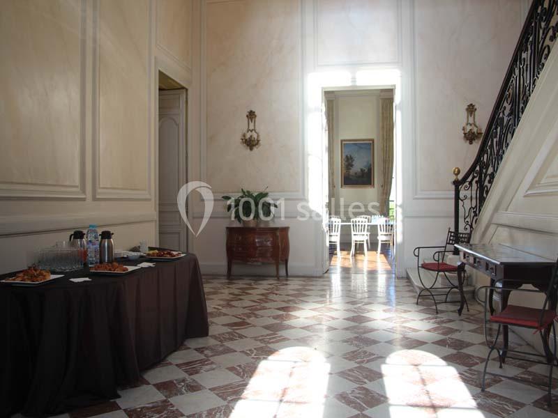 Salle lumineuse avec sol en marbre, table de buffet à gauche, escalier à droite et vue sur une autre pièce au fond.