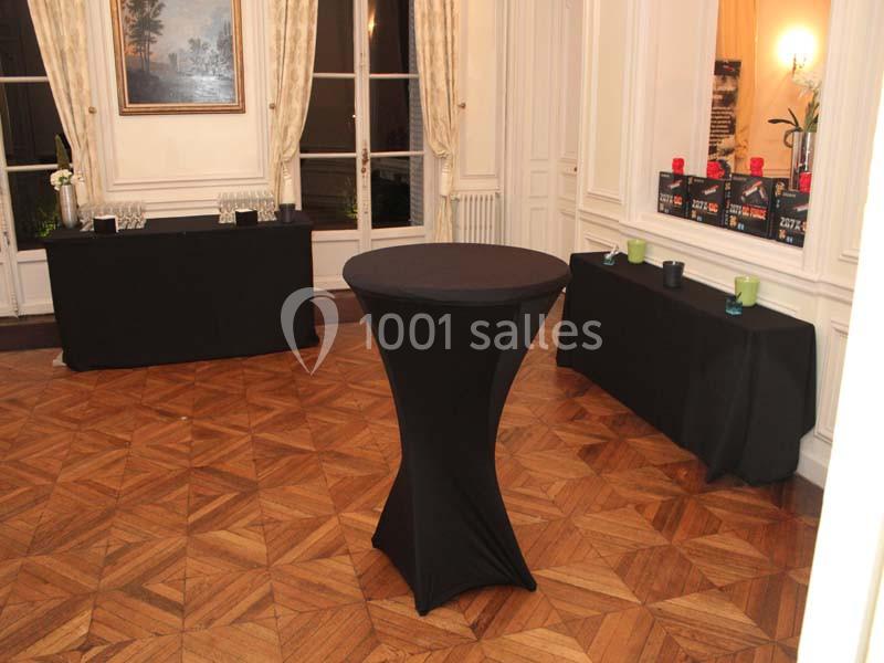 Salle avec parquet, tables recouvertes de nappes noires, bougies et verres disposés pour un événement.