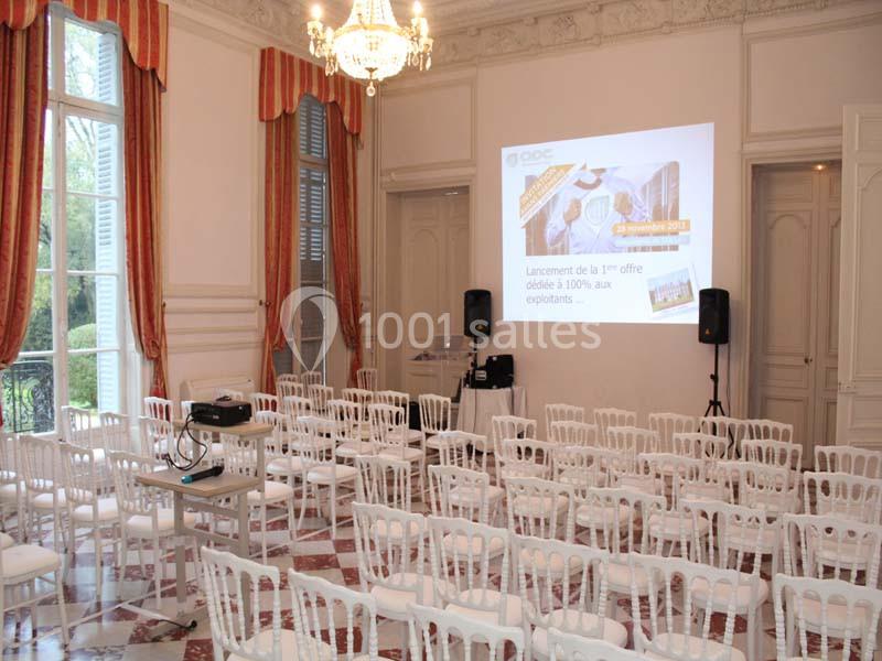 Salle de conférence lumineuse avec des chaises blanches alignées et un projecteur affichant une présentation sur un écran.