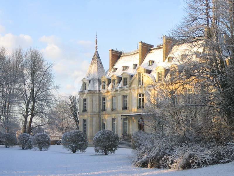 Château entouré d'arbres et de buissons sous la neige, éclairé par une lumière douce en hiver.
