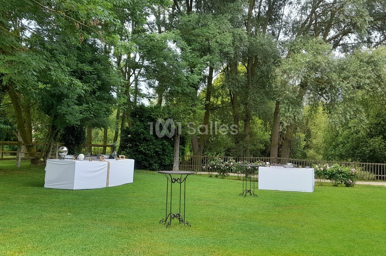 Tables de buffet dressées sur une pelouse verte entourée d'arbres dans un cadre extérieur paisible.