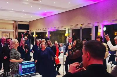 Miniature DJ Bondues (Nord) - Luk Event #7 Des personnes dansent et chantent dans une salle éclairée de lumières colorées, avec un chanteur au premier plan.