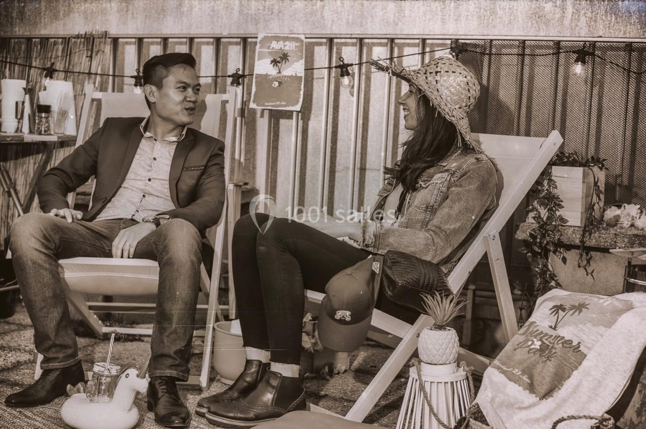 Un homme et une femme discutent assis sur des chaises longues dans un décor extérieur décontracté.