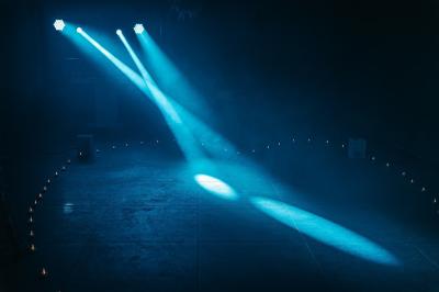 Personnes dansant sous des lumières colorées dans une salle sombre avec une scène équipée de matériel de DJ.