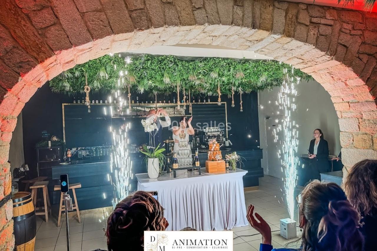 Deux personnes derrière un bar décoré, entourées d'étincelles et d'une arche en pierre, lors d'un événement festif.