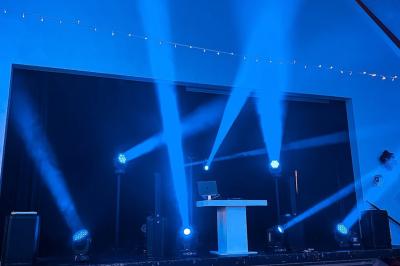 Personnes dansant sous des lumières colorées dans une salle sombre avec une scène équipée de matériel de DJ.