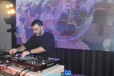 Personnes dansant sous des lumières colorées dans une salle sombre avec une scène équipée de matériel de DJ.