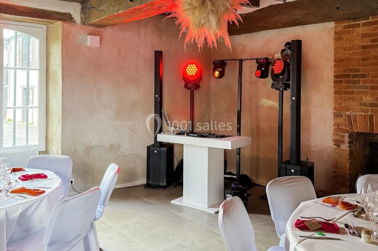 Table de mixage et éclairage rouge installés dans une salle de réception avec murs en pierre et tables dressées.