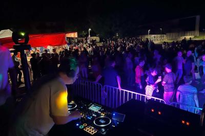 Un DJ mixant de la musique sur une table de mixage éclairée par des lumières colorées dans une ambiance sombre.