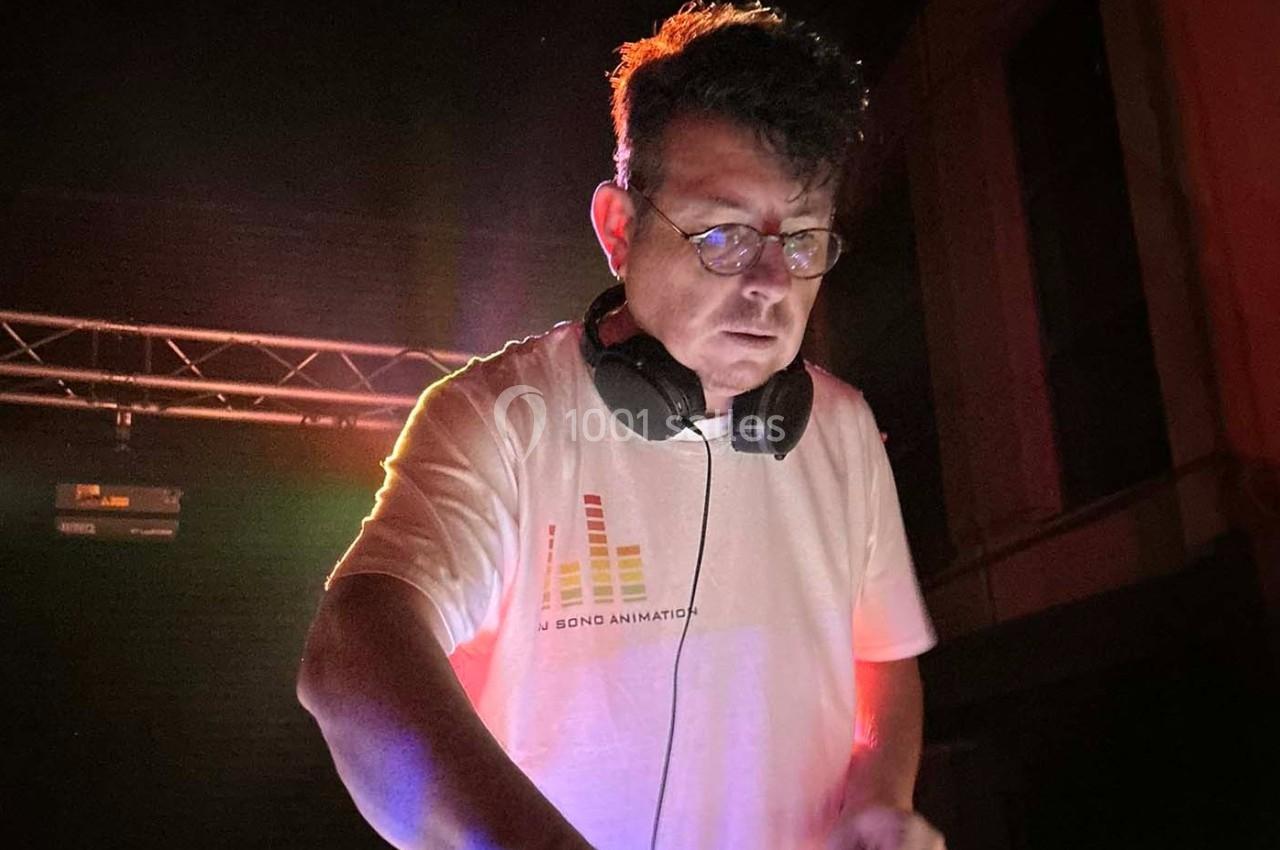 Un DJ portant un casque audio mixe de la musique sous un éclairage coloré dans un environnement sombre.