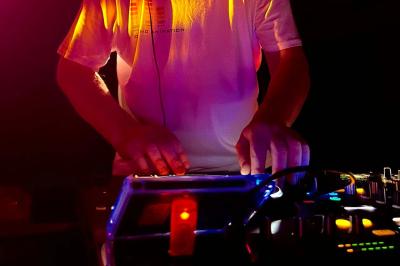 Un DJ mixant de la musique sur une table de mixage éclairée par des lumières colorées dans une ambiance sombre.