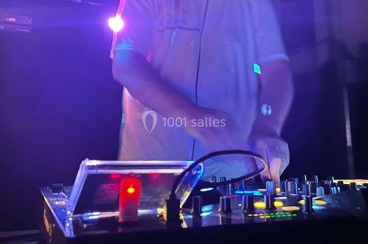 Un DJ mixant de la musique sur une table de mixage éclairée par des lumières colorées dans une ambiance sombre.