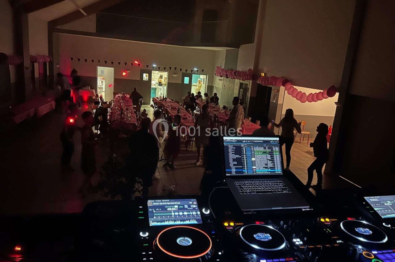 Salle de fête décorée avec des guirlandes, des invités dansant et une table de mixage en premier plan.