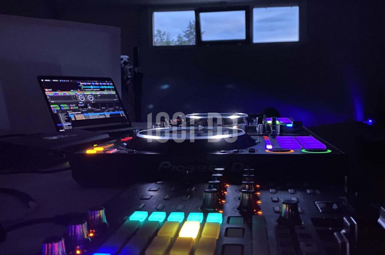 Table de mixage éclairée avec des boutons colorés, un ordinateur portable affichant un logiciel DJ et une fenêtre en arrière…