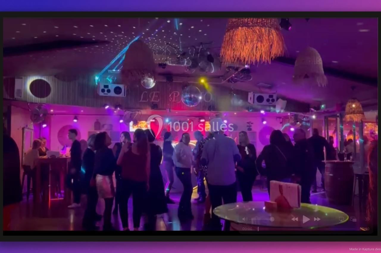Groupe de personnes dans une salle de fête éclairée par des lumières colorées, avec un bar en arrière-plan.