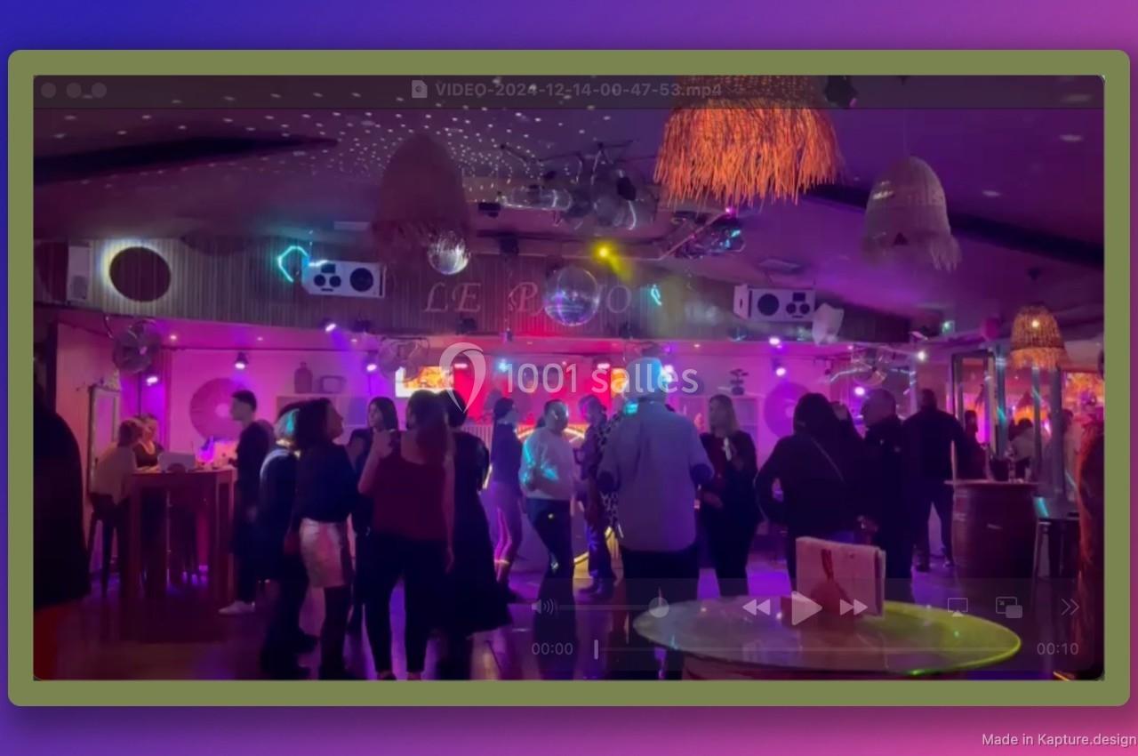 Personnes dansant dans une salle éclairée par des lumières colorées, avec un bar et une décoration festive en arrière-plan.