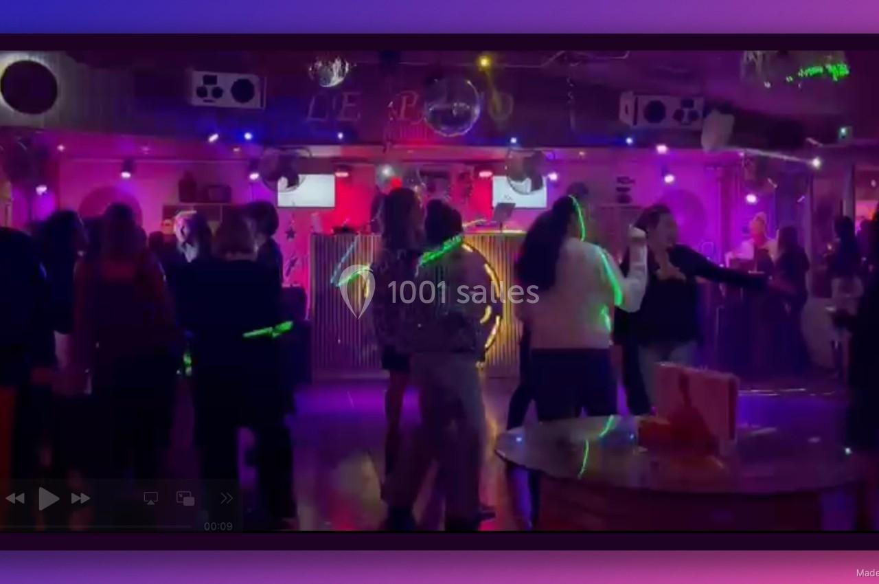 Des personnes dansent dans une salle de fête éclairée par des lumières colorées et des projecteurs.