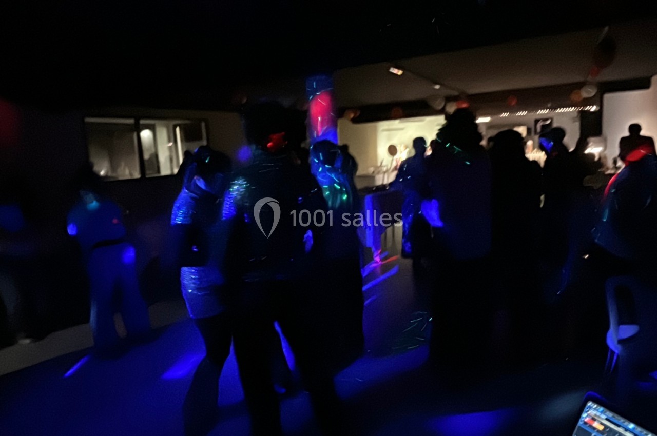 Personnes dansant dans une salle sombre éclairée par des lumières colorées, ambiance festive en soirée.
