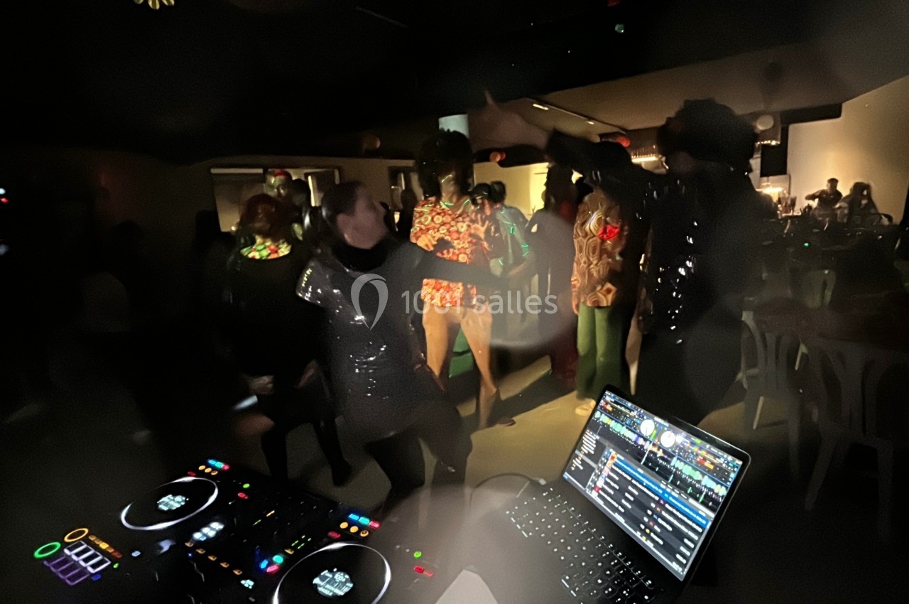 Personnes dansant dans une ambiance festive et sombre, avec une table de mixage et un ordinateur au premier plan.