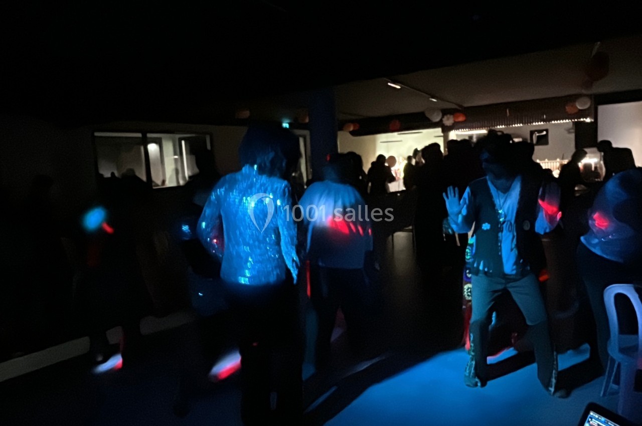 Personnes dansant dans une salle sombre éclairée par des lumières colorées, ambiance festive.