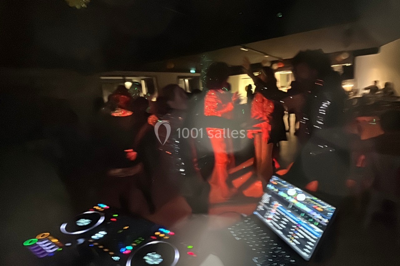 Personnes dansant dans une ambiance festive et tamisée, avec une table de mixage DJ visible au premier plan.