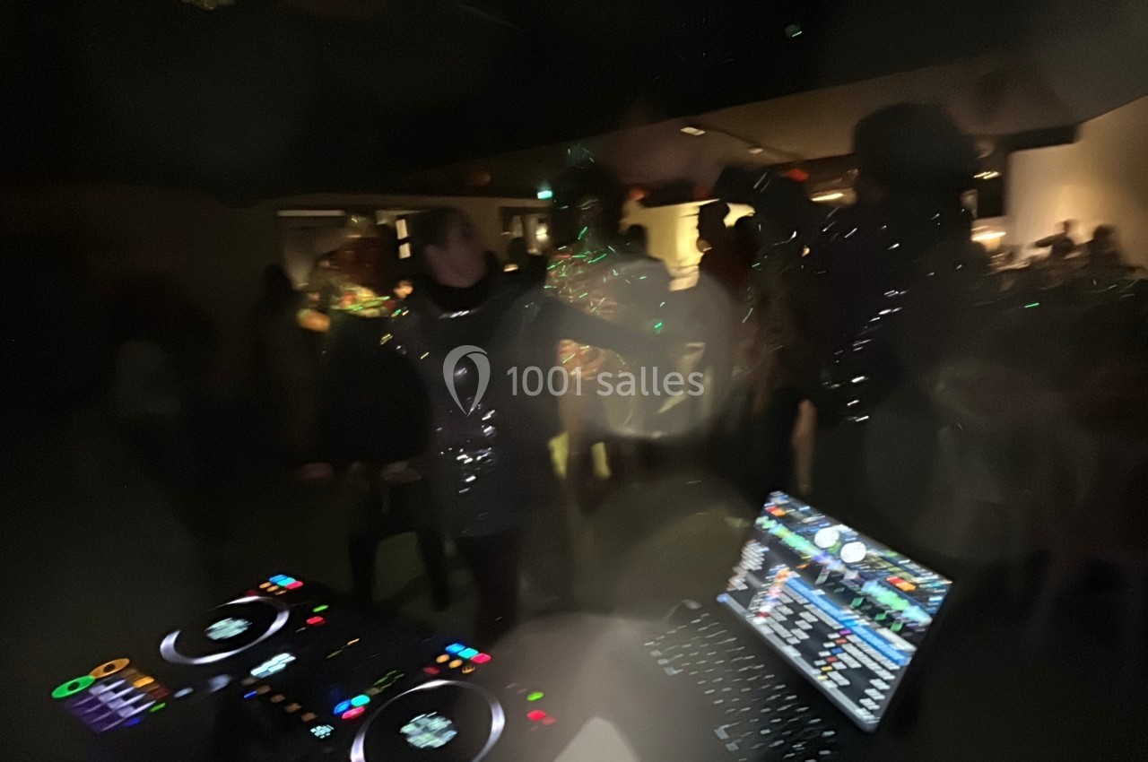Personnes dansant dans une ambiance sombre avec des lumières scintillantes, vue partielle d'une console de DJ au premier…