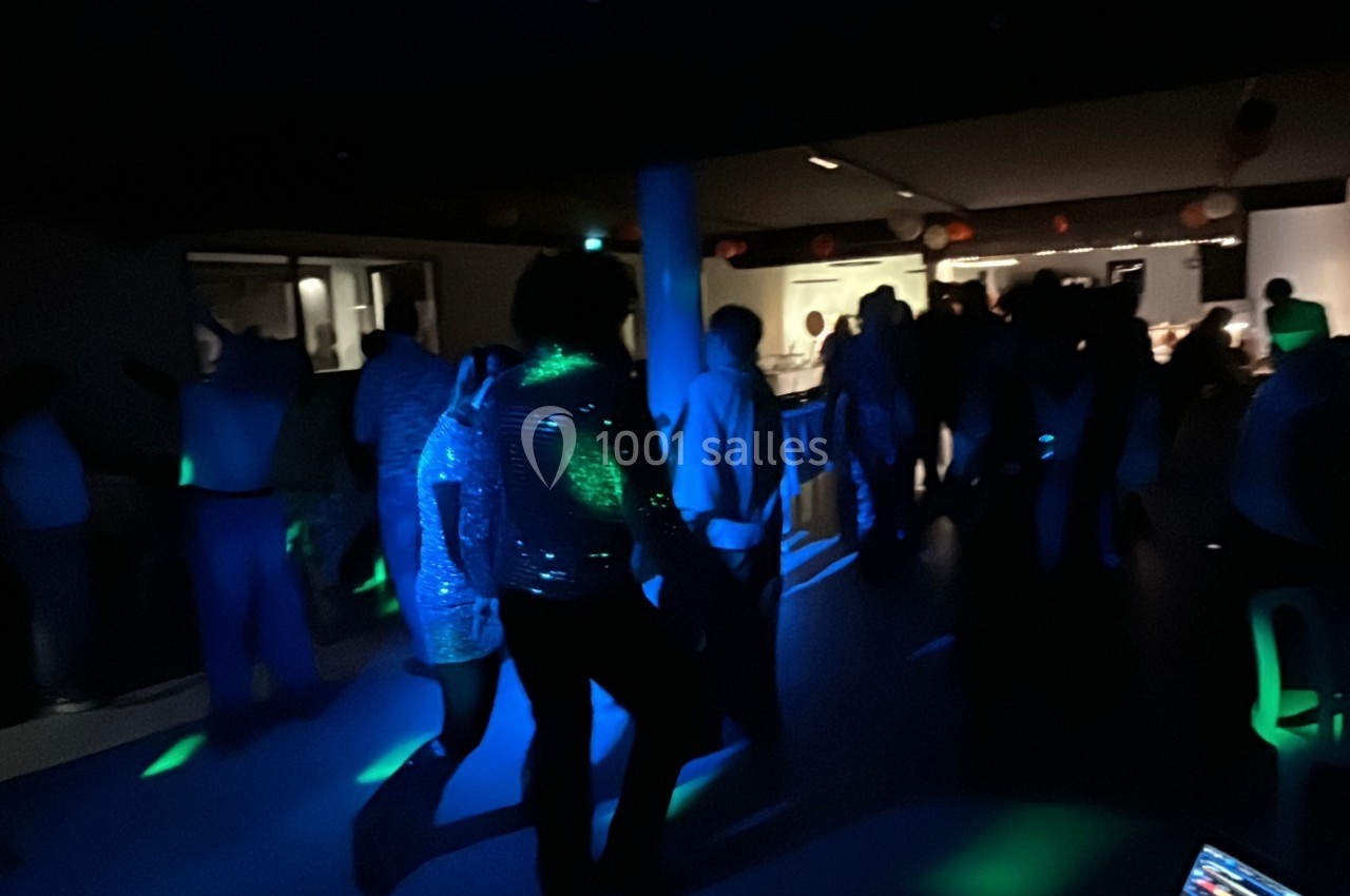 Des personnes dansent dans une salle faiblement éclairée avec des lumières colorées et une ambiance festive.