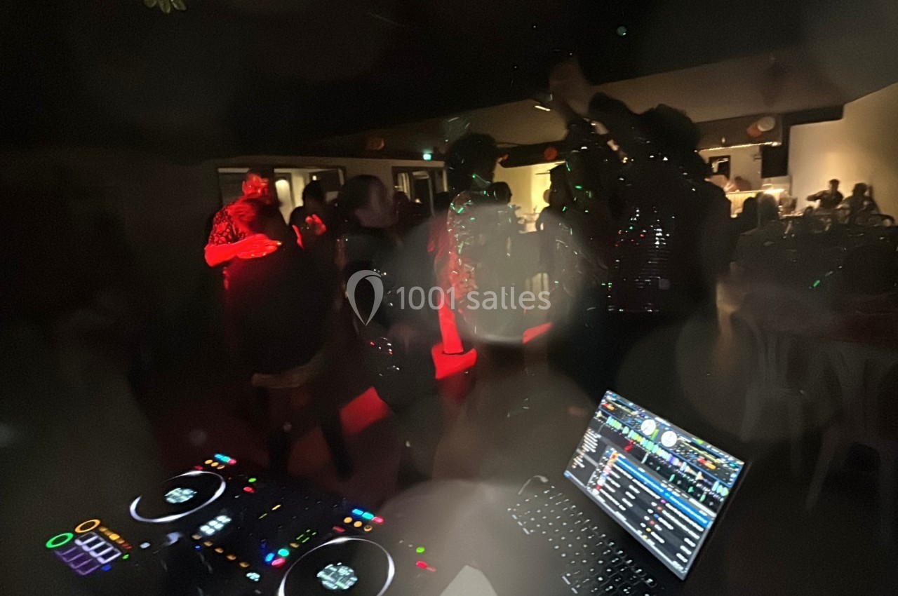 Des personnes dansent dans une ambiance sombre et lumineuse, avec une table de mixage visible au premier plan.