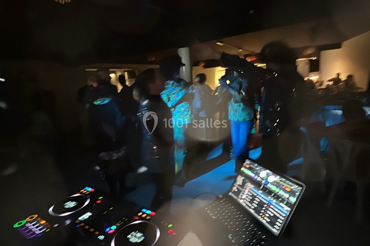 Vue floue d'une soirée avec des personnes dansant sous des lumières tamisées, tables et platines de DJ au premier plan.