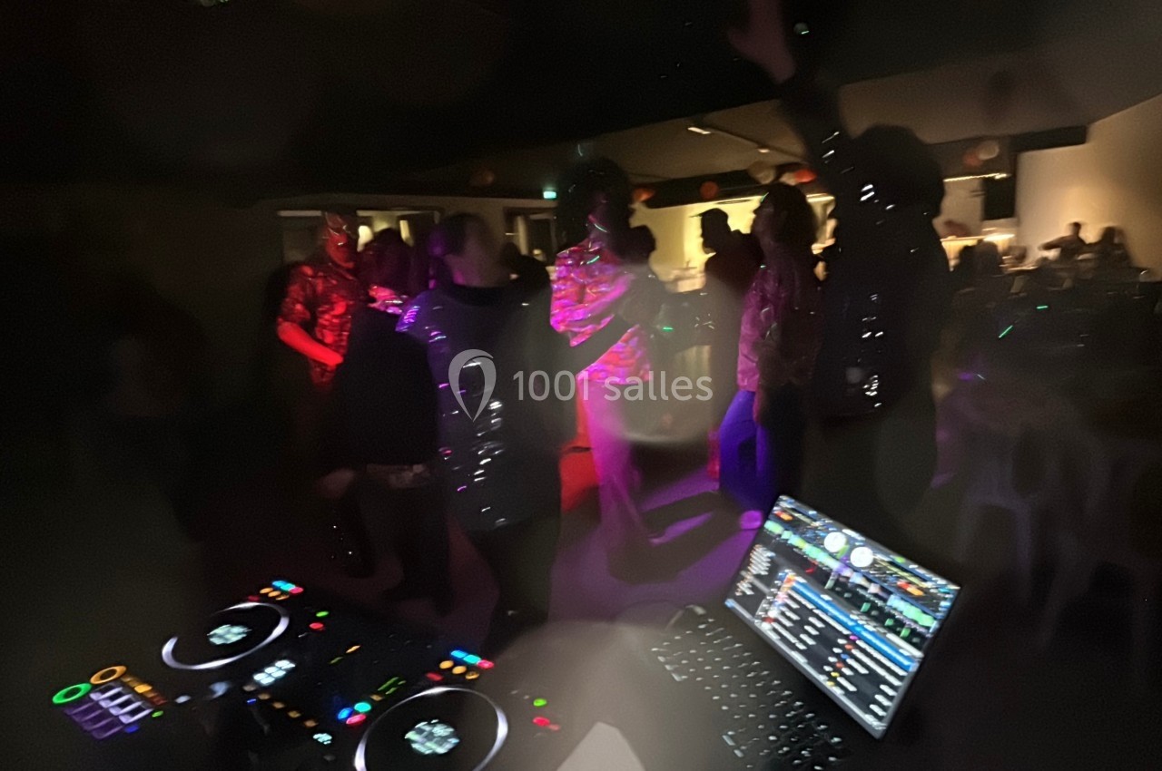 Personnes dansant dans une ambiance festive avec des lumières colorées, vue depuis une table de mixage de DJ.