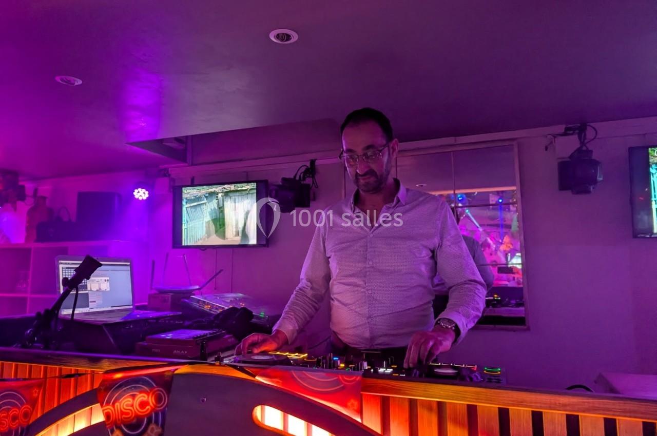 Un DJ mixe de la musique dans un club éclairé par des lumières violettes, avec des écrans en arrière-plan.