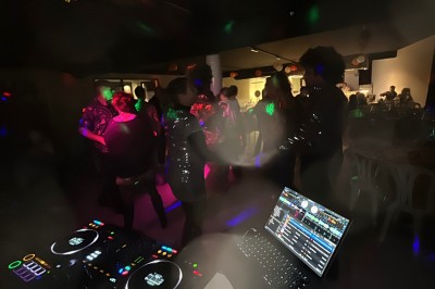 Personnes dansant dans une salle sombre éclairée par des lumières colorées, ambiance festive.